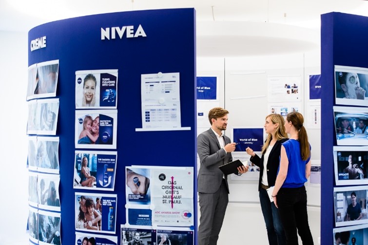 Three Millennials talking in front of a blue wall with Nivea brand logo